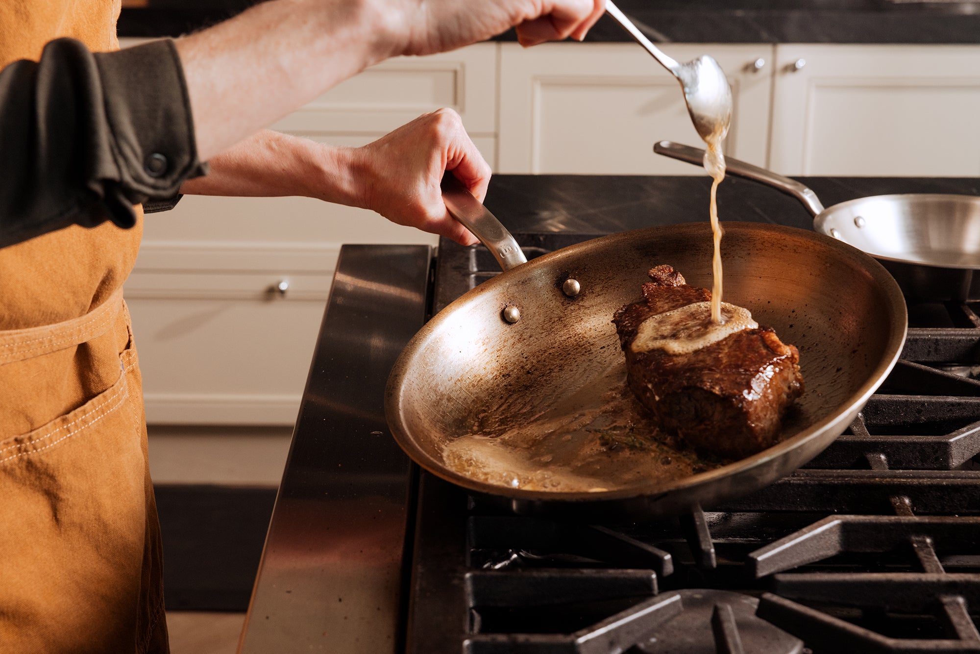 A steak is basted in a Made In Stainless Clad Frying Pan.