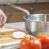 A Made In Stainless Clad Saucier sits on a countertop. Alongside it, a person cuts an onion.