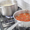 A Made In Stainless Clad Saute Pan on a stove top alongside a pot of noodles in boiling water. Meatballs and sauce are being cooked in the saute pan.
