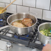 A Made In Stainless Clad Saute Pan on a stove top alongside two saucepans of other foods. Pork chops are being cooked in the saute pan.