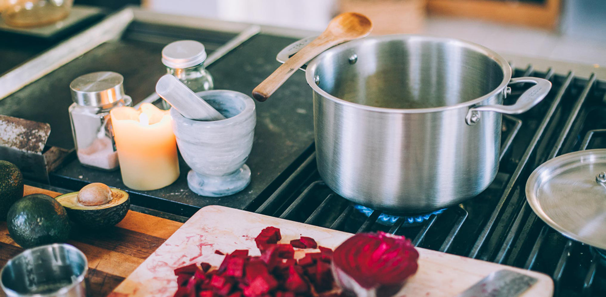 A Made In Stainless Clad Stock Pot on a stove top alongside ingredients and other cooking tools.