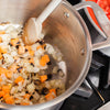 A Made In Stainless Clad Stock Pot on a stovetop. Diced aromatics and vegetables are being cooked in the pot.