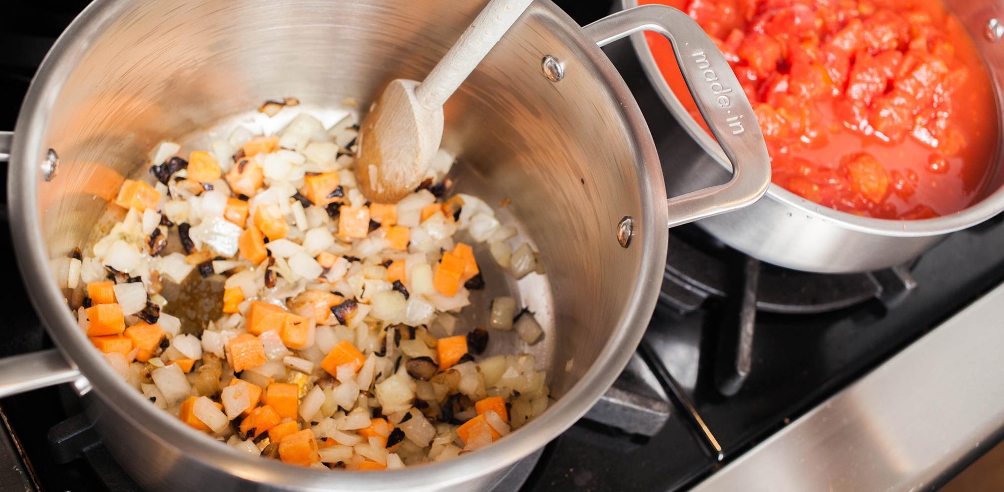 A Made In Stainless Clad Stock Pot on a stovetop. Diced aromatics and vegetables are being cooked in the pot.