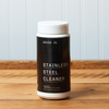 A bottle of Made In's Stainless Steel Cleaner sits on a wooden table.