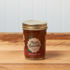 A jar of Maine Homestead Apple Pie Jam sits on a brown wooden table.