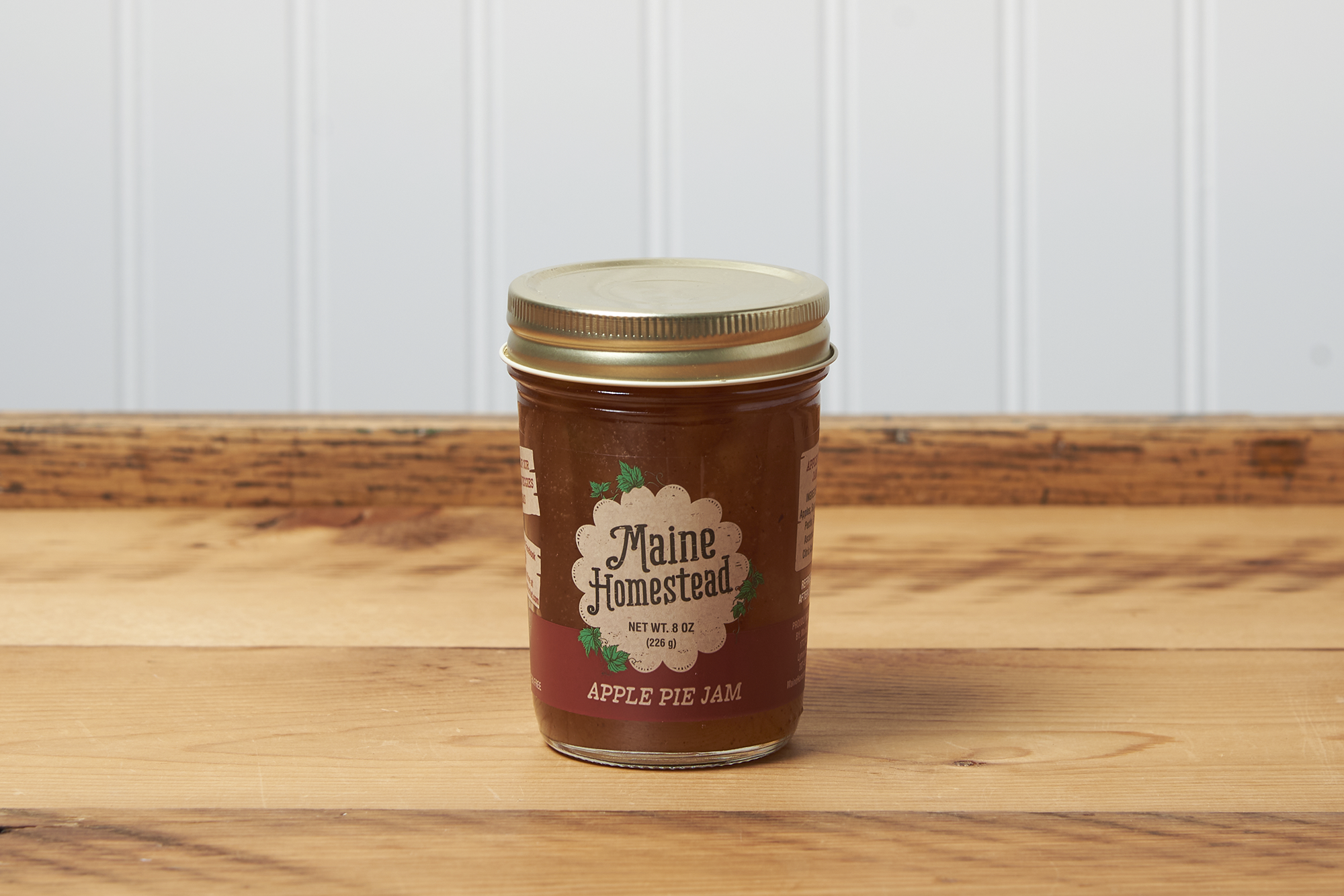 A jar of Maine Homestead Apple Pie Jam sits on a brown wooden table.