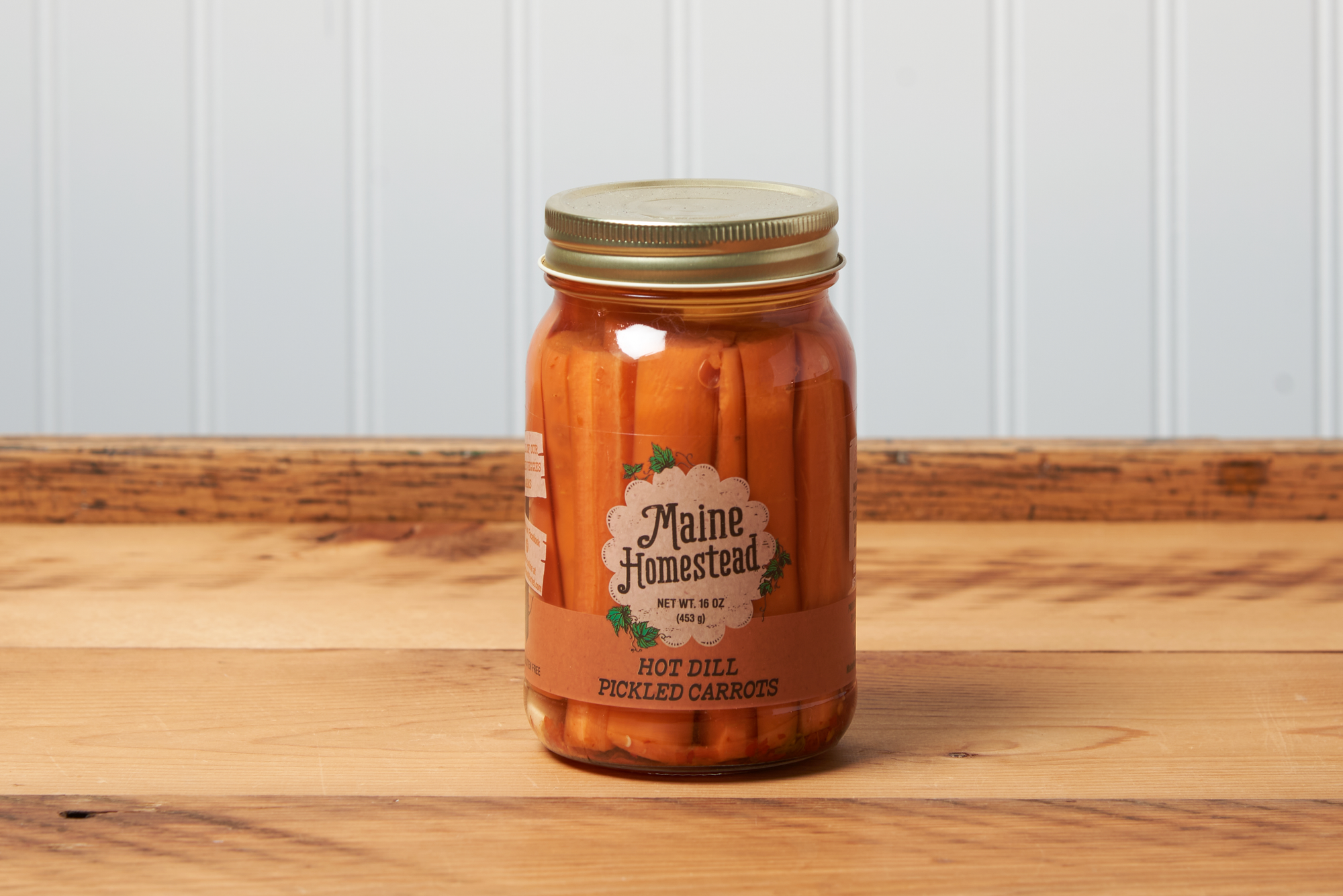 A jar of Maine Homestead Hot Dill Pickled Carrots sits on a brown wooden table.