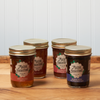 Four jars of assorted Maine Homestead jams and jelly sit on a brown wooden table.