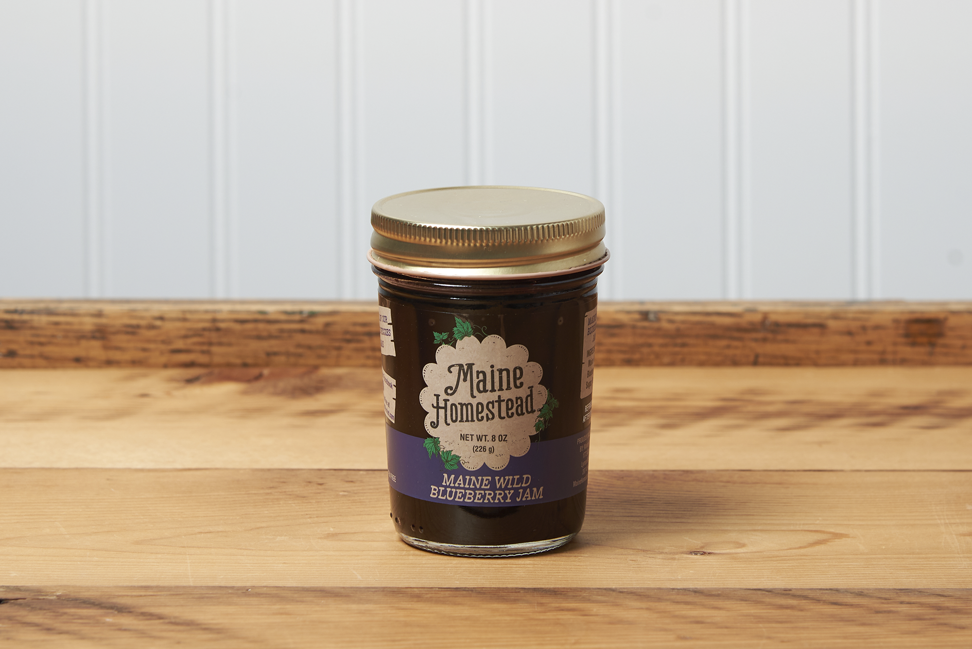 A jar of Maine Homestead Wild Maine Blueberry Jam sits on a brown wooden table.