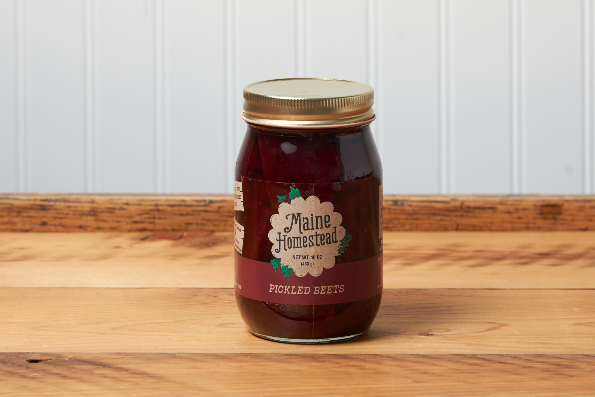 A jar of Maine Homestead Pickled Beets sits on a brown wooden table.