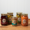 Five jars of assorted Maine Homestead pickled vegetables sit on a brown wooden table.