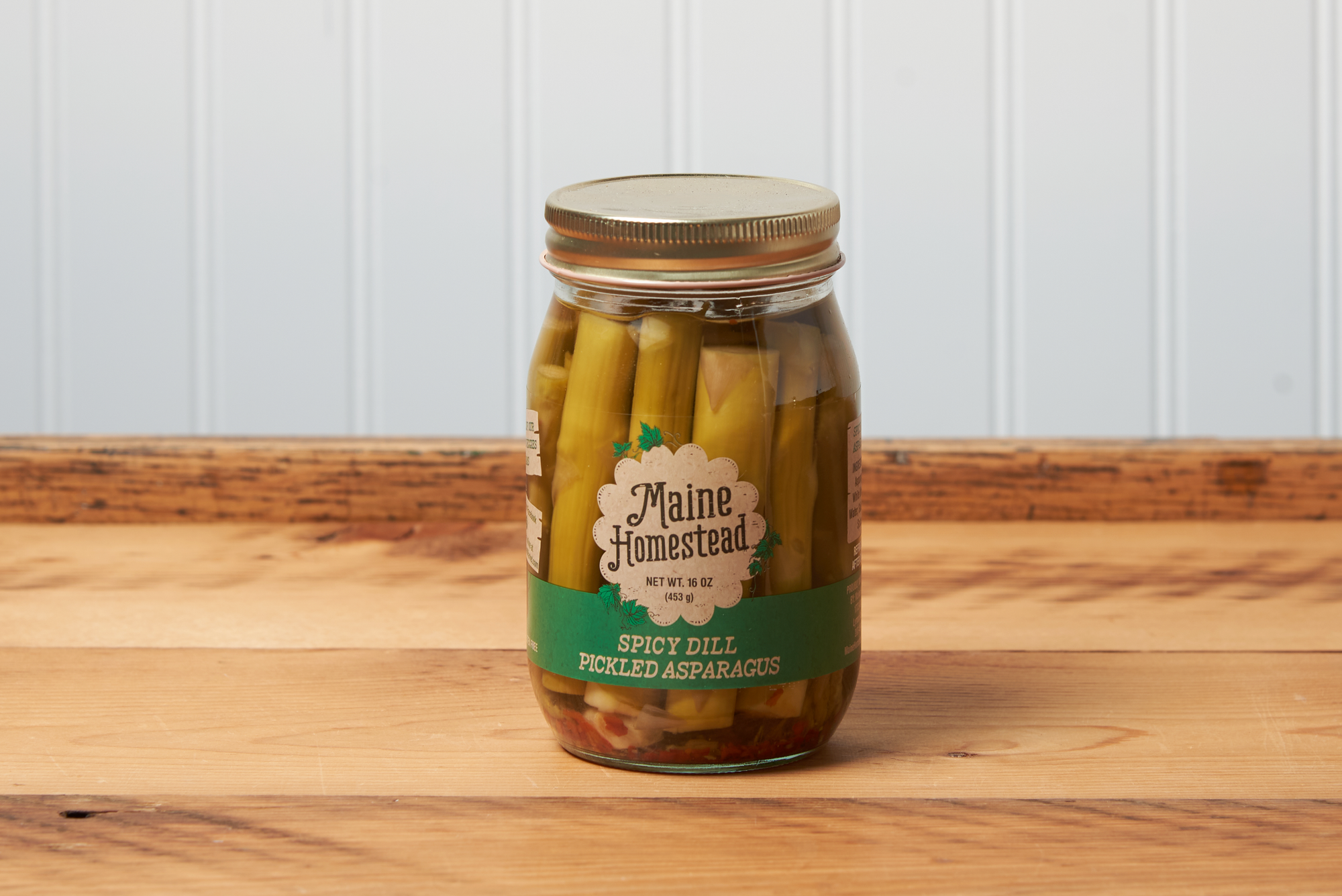 A jar of Maine Homestead Spicy Dill Pickled Asparagus sits on a brown wooden table.