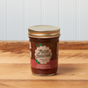 A jar of Maine Homestead Strawberry Rhubarb Jam sits on a brown wooden table.
