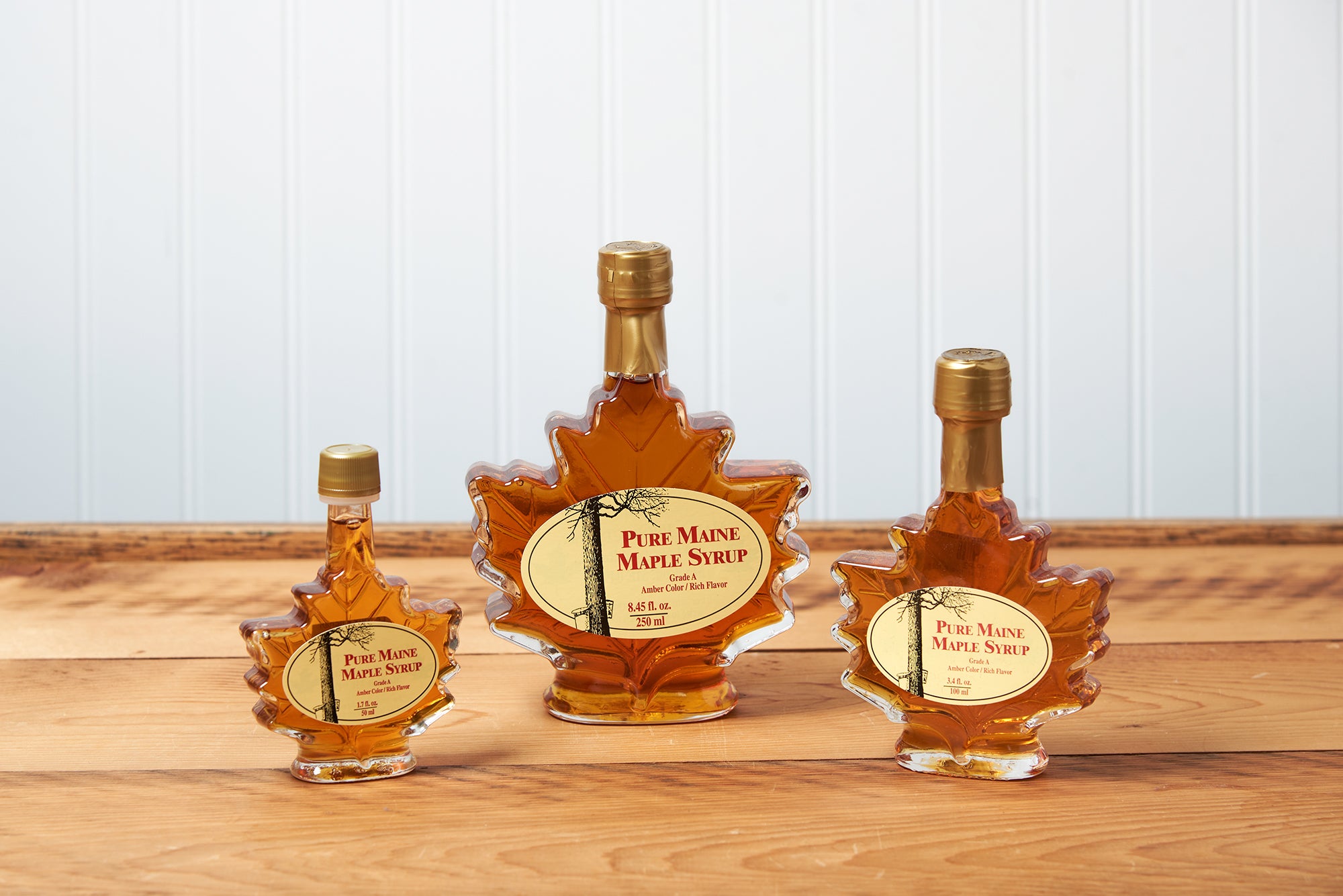 Three Maine Maple Syrup maple leaf jars sit on a brown wooden table.