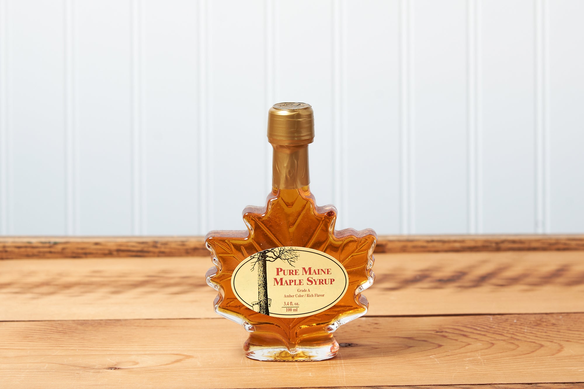 A 100ml Maine Maple Syrup maple leaf jar sits on a brown wooden table.