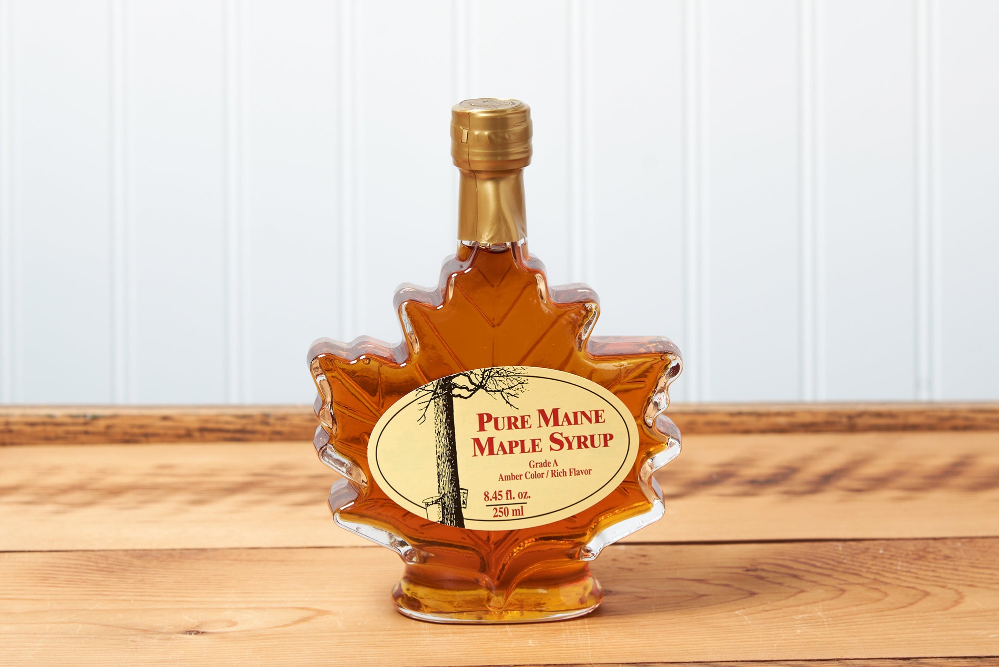 An 8 ounce Maine Maple Syrup maple leaf jar sits on a brown wooden table.