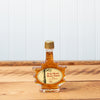 A 50ml Maine Maple Syrup maple leaf jar sits on a brown wooden table.