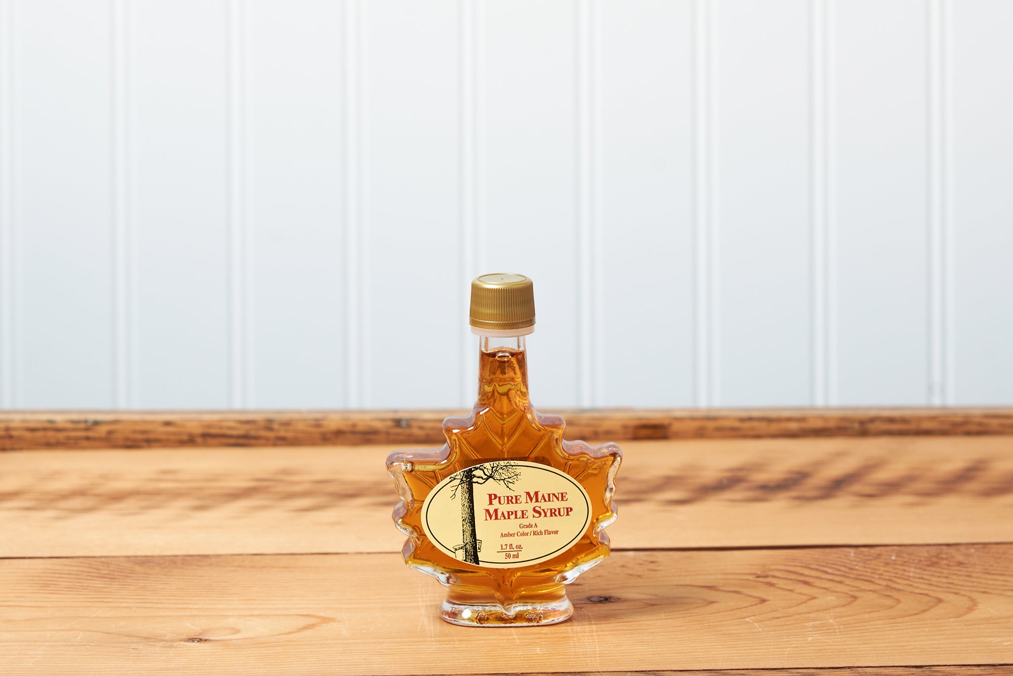 A 50ml Maine Maple Syrup maple leaf jar sits on a brown wooden table.