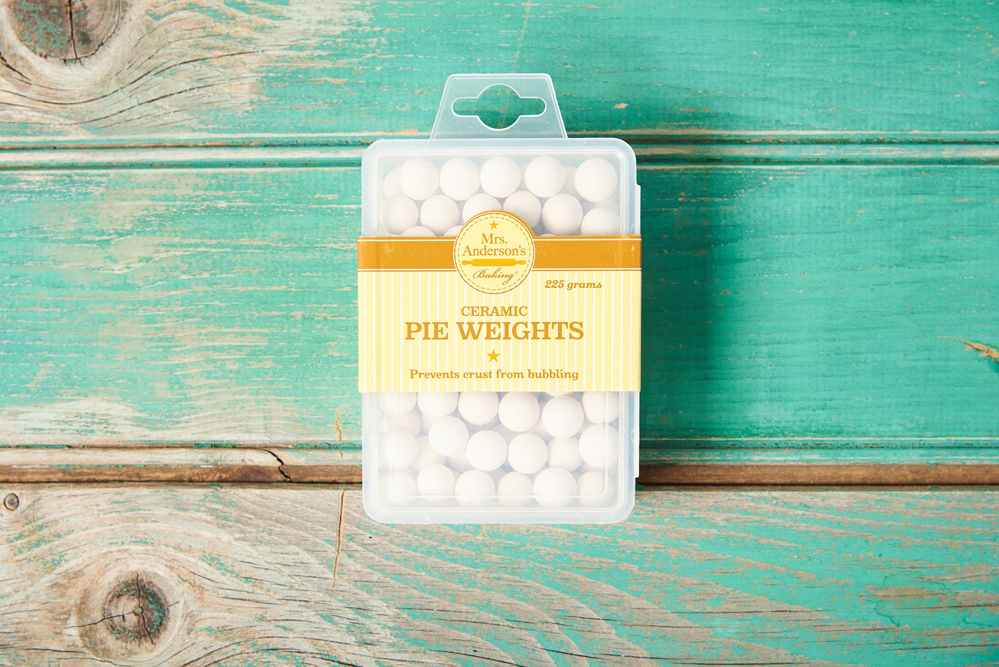 A package of Mrs. Anderson's Baking Ceramic Pie Weights sits on a turquoise wooden tabletop.