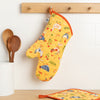 A Now Designs Free Range Oven Mitt hangs on a kitchen wall.