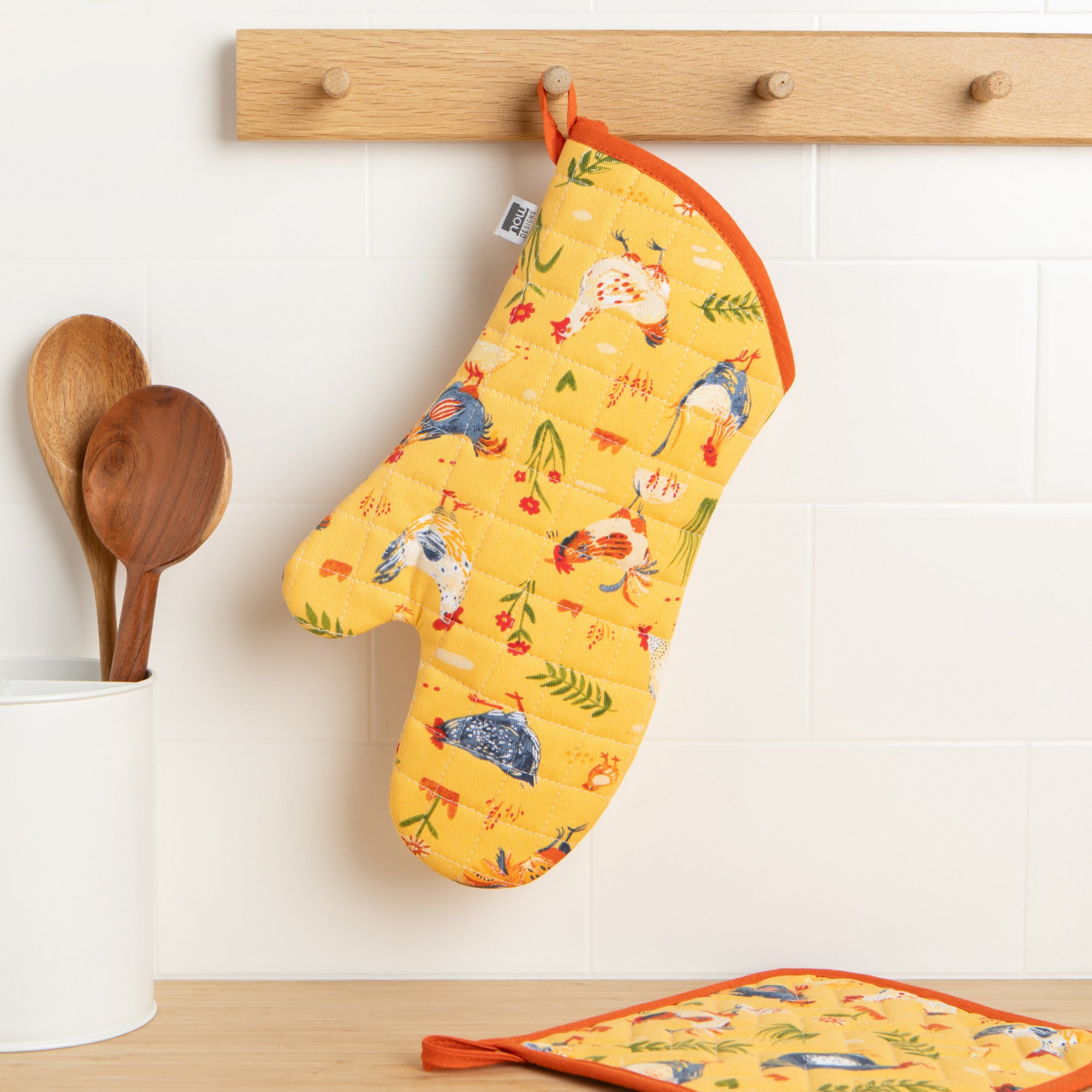 A Now Designs Free Range Oven Mitt hangs on a kitchen wall.