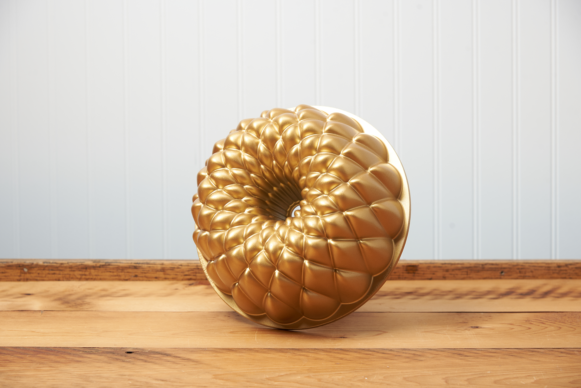 A Nordic Ware Kaleidoscope Bundt Pan sits on a brown, wooden table.