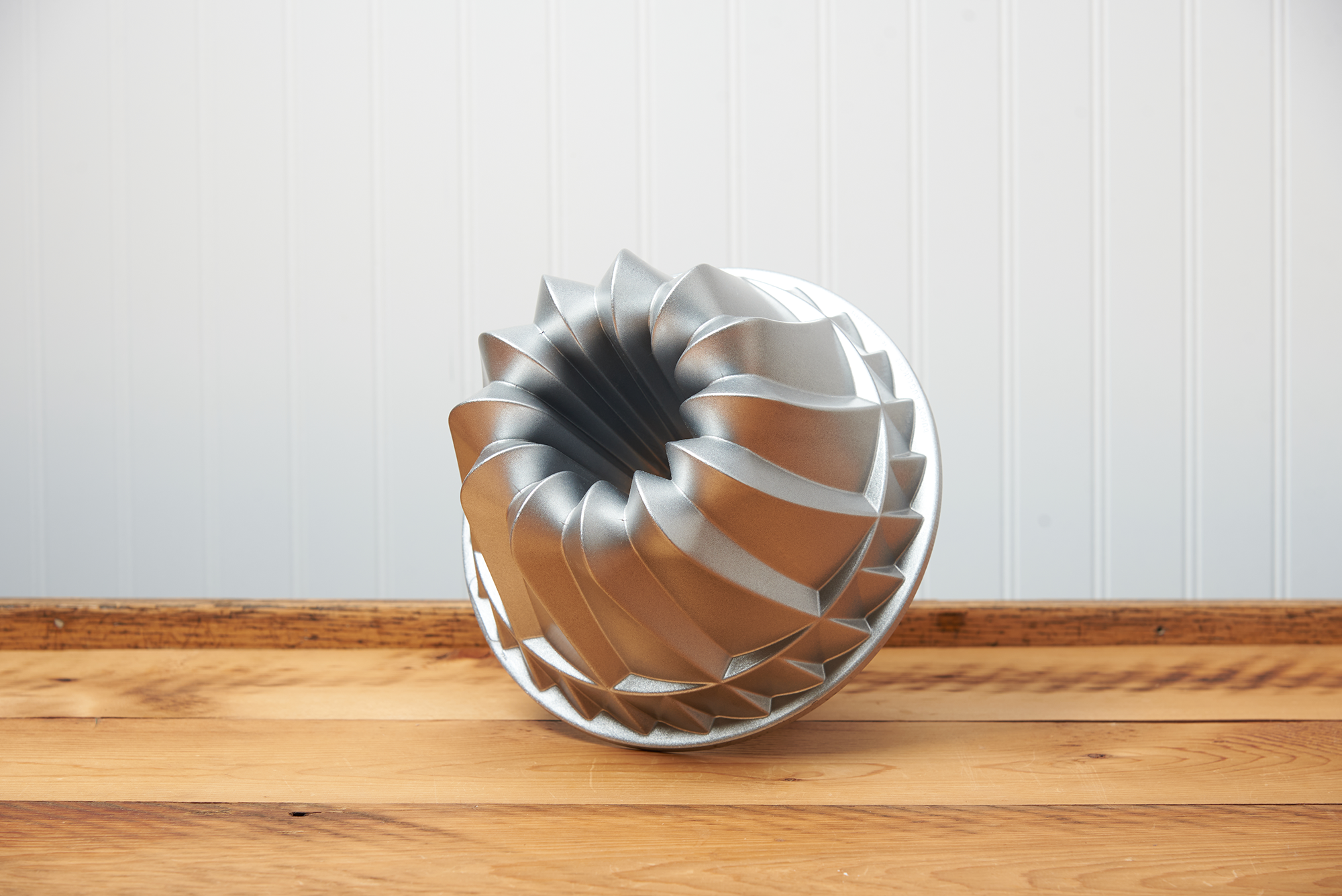 A Nordic Ware Kugelhopf Bundt Pan sits on a brown, wooden table.