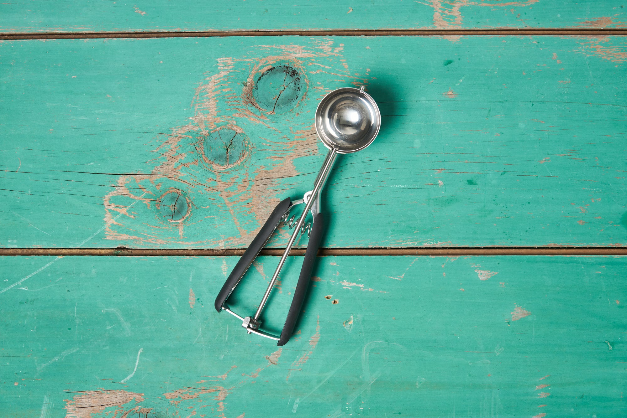 A size large OXO Cookie Scoop sits on a turquoise wooden tabletop.