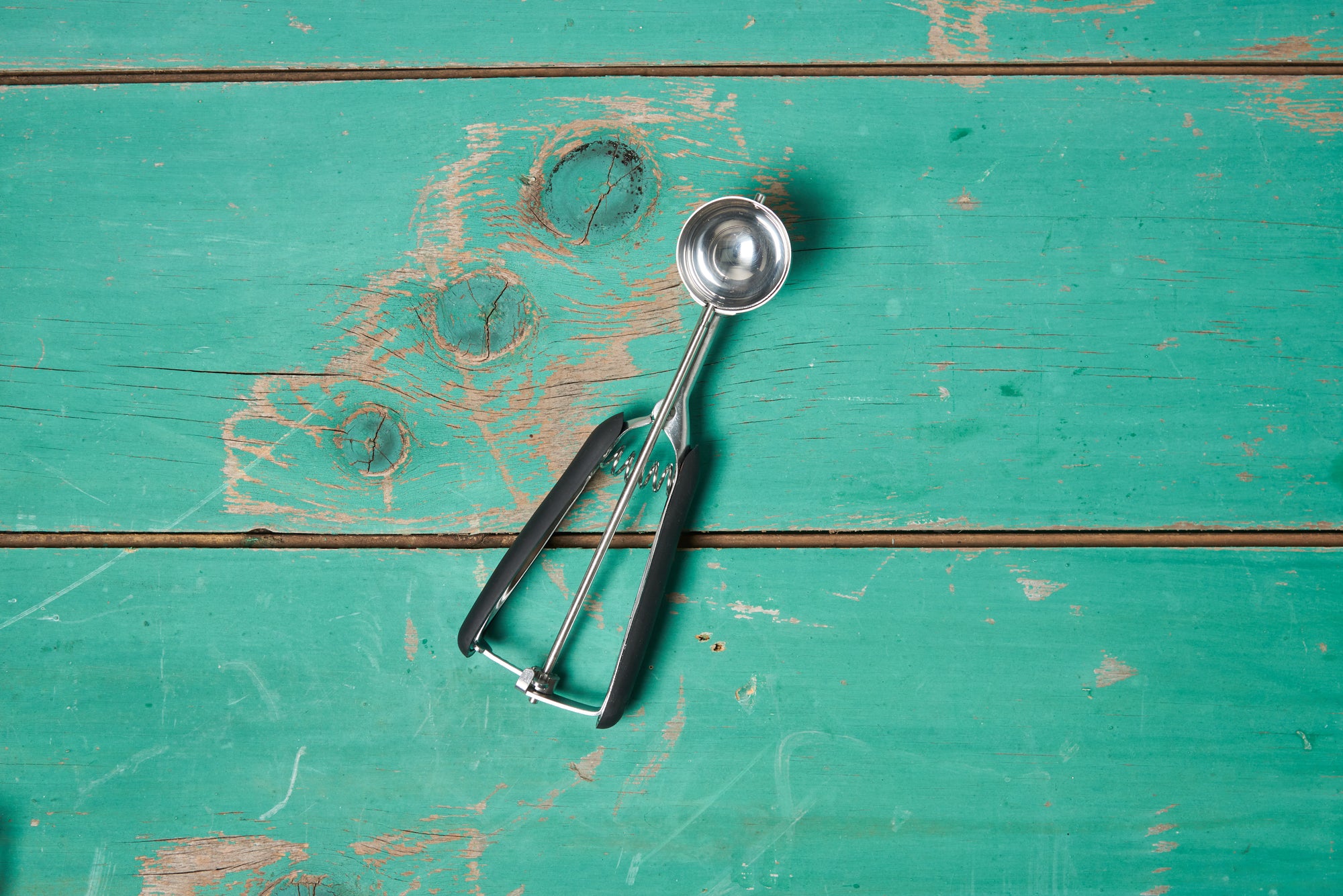 A size medium OXO Cookie Scoop sits on a turquoise wooden tabletop.