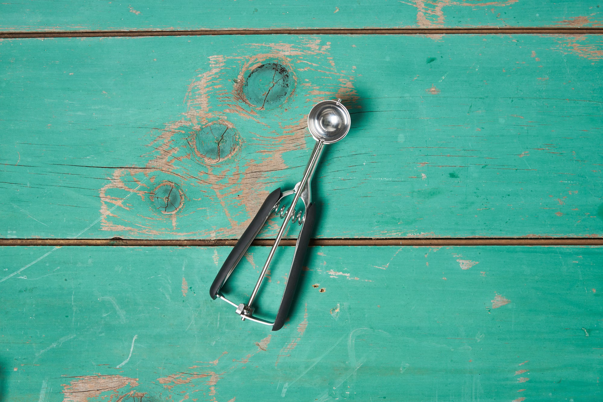 A size small OXO Cookie Scoop sits on a turquoise wooden tabletop.