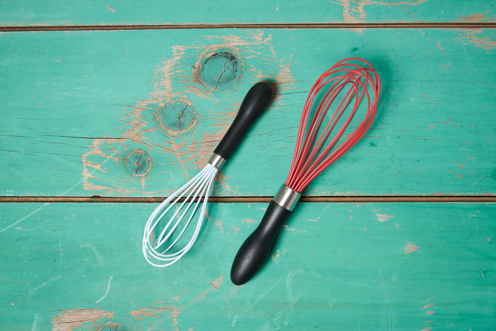 An OXO Silicone Whisks, Set of 2 sits on a turquoise wooden tabletop.