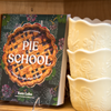 The cookbook 'Pie School: Lessons in Fruit, Flour & Butter' sits on a shelf alongside floral embellished bakeware.