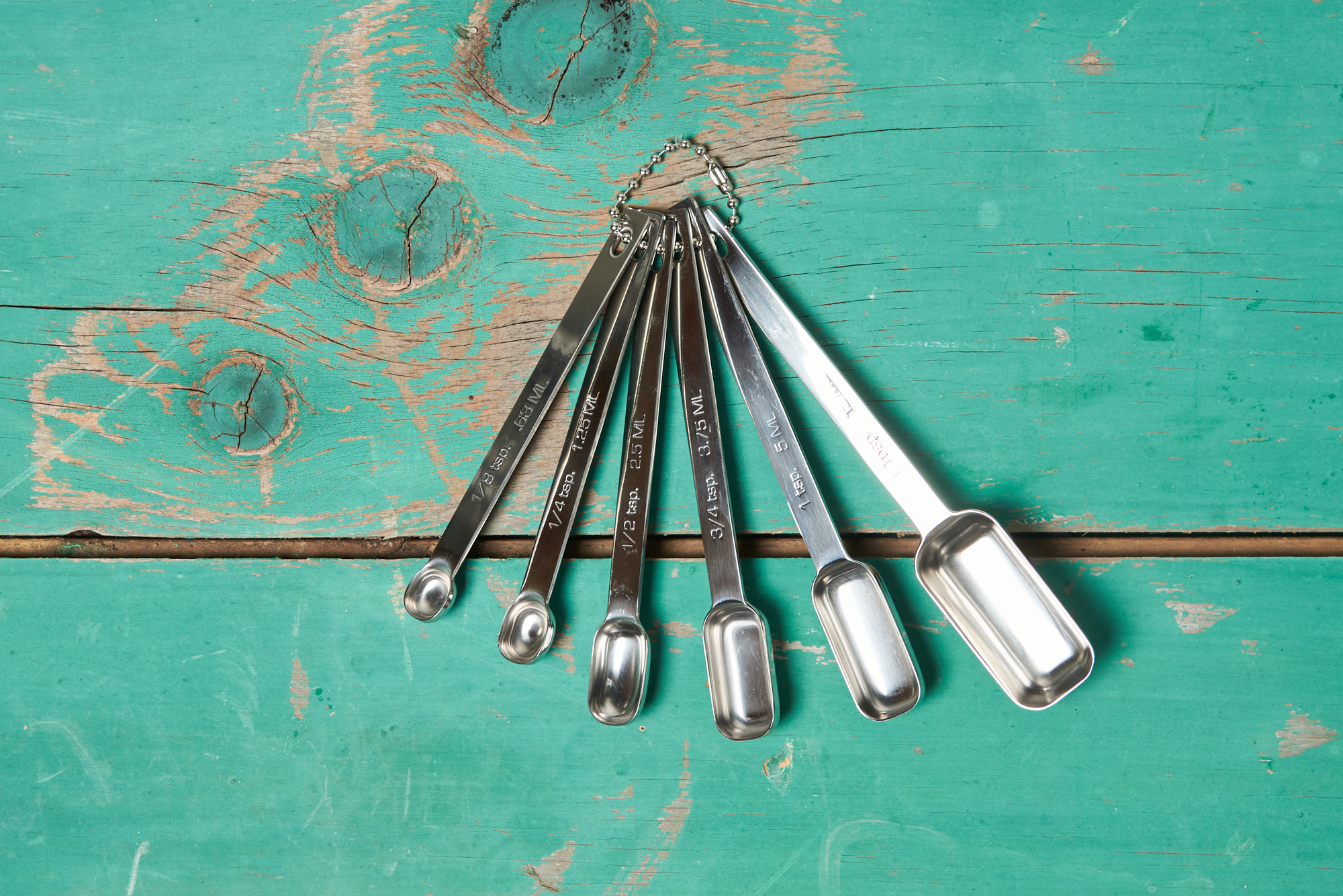 An RSVP Endurance Spice Measuring Spoons, Set of 6 on a turquoise tabletop.