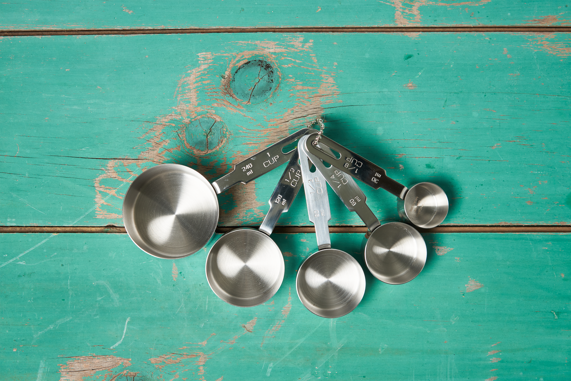 An RSVP Endurance Measuring Cups, Set of 5 on a turquoise wooden tabletop.