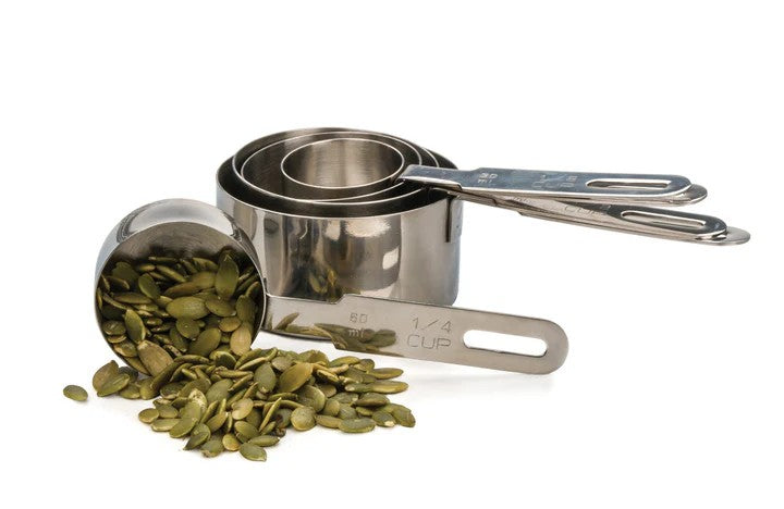 An RSVP Endurance Measuring Cups, Set of 5 over a white background. One cup is turned on its side, with seeds tumbling out.