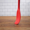 A red RSVP Ela's Favorite Silicone Spoon is pressed against a wooden countertop.