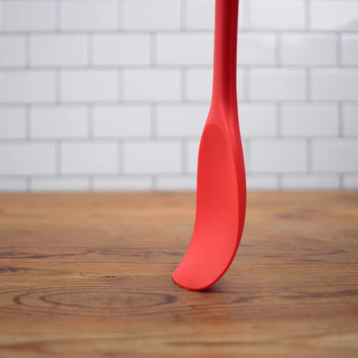 A red RSVP Ela's Favorite Silicone Spoon is pressed against a wooden countertop.