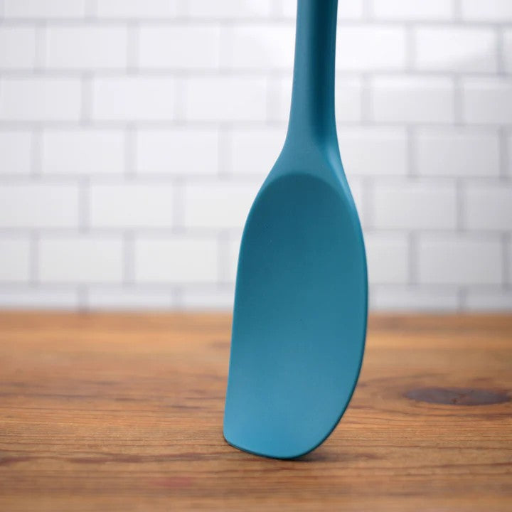 A turquoise RSVP Ela's Favorite Silicone Spoon is pressed against a wooden countertop.