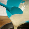A turquoise RSVP Ela's Favorite Silicone Spoon is used to empty batter from a bowl.