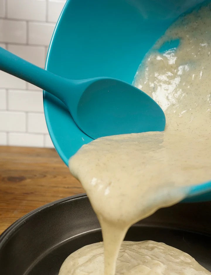 A turquoise RSVP Ela's Favorite Silicone Spoon is used to empty batter from a bowl.