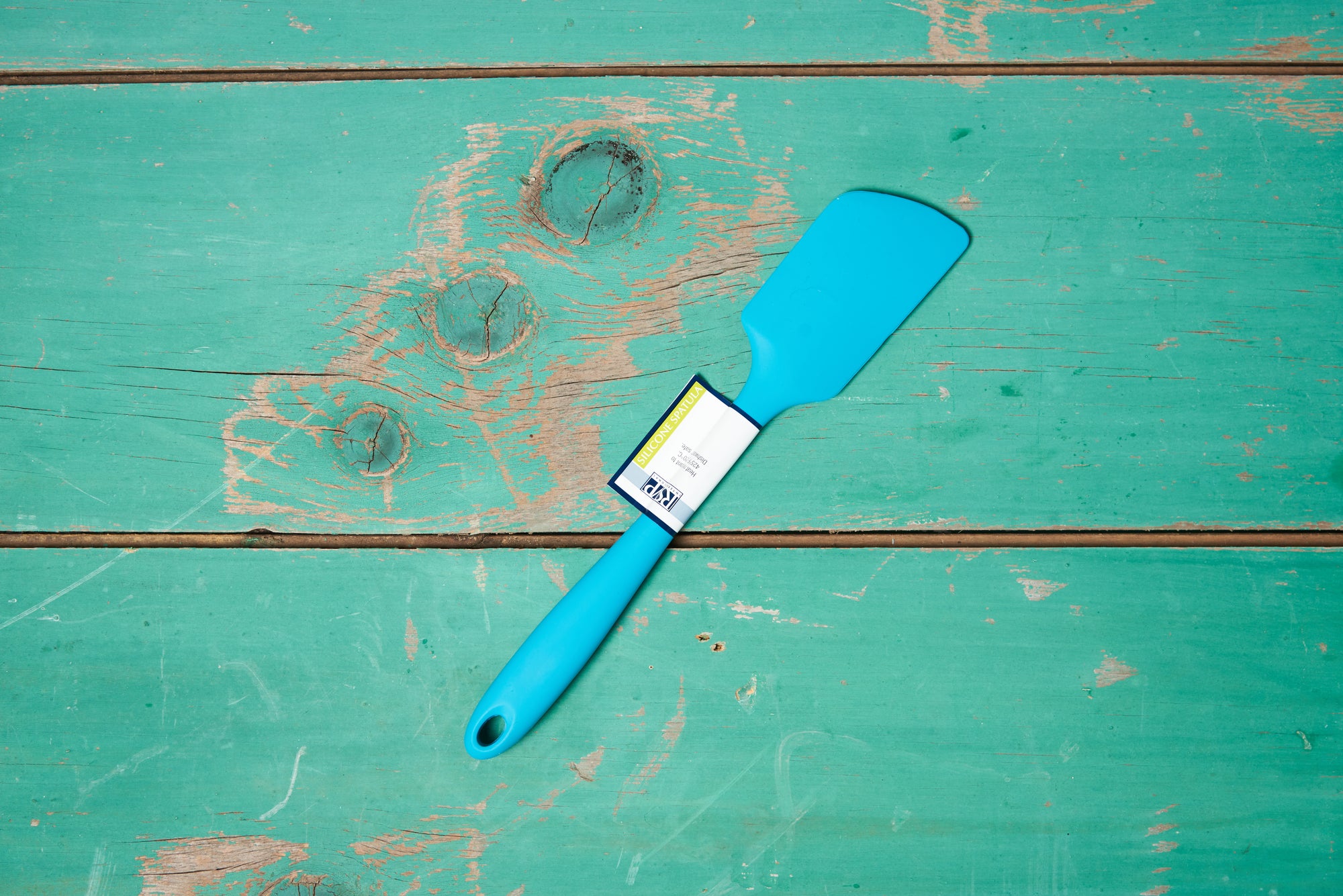 A turquoise Ela's Favorite Silicone Spoon sits on a turquoise tabletop.