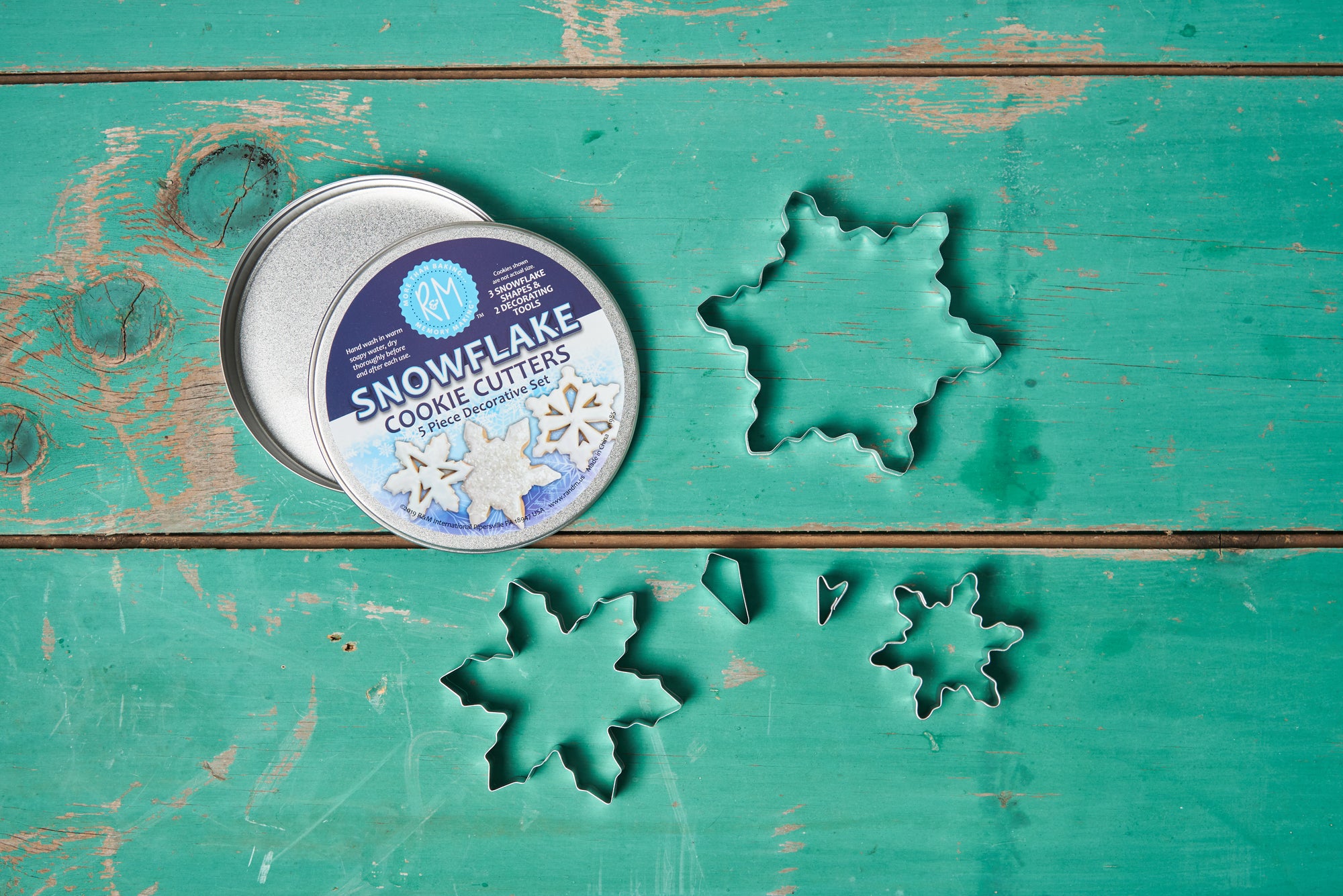An R&M International Snowflake Cookie Cutters, Set of 5 is scattered on a turquoise wooden tabletop.