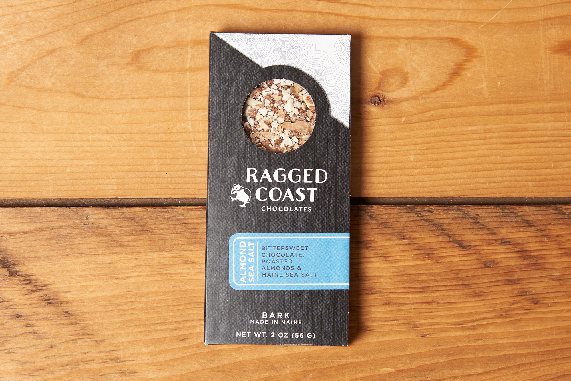 One Ragged Coast Chocolates Chocolate Almond and Maine Sea Salt Bark sits on a wooden table.