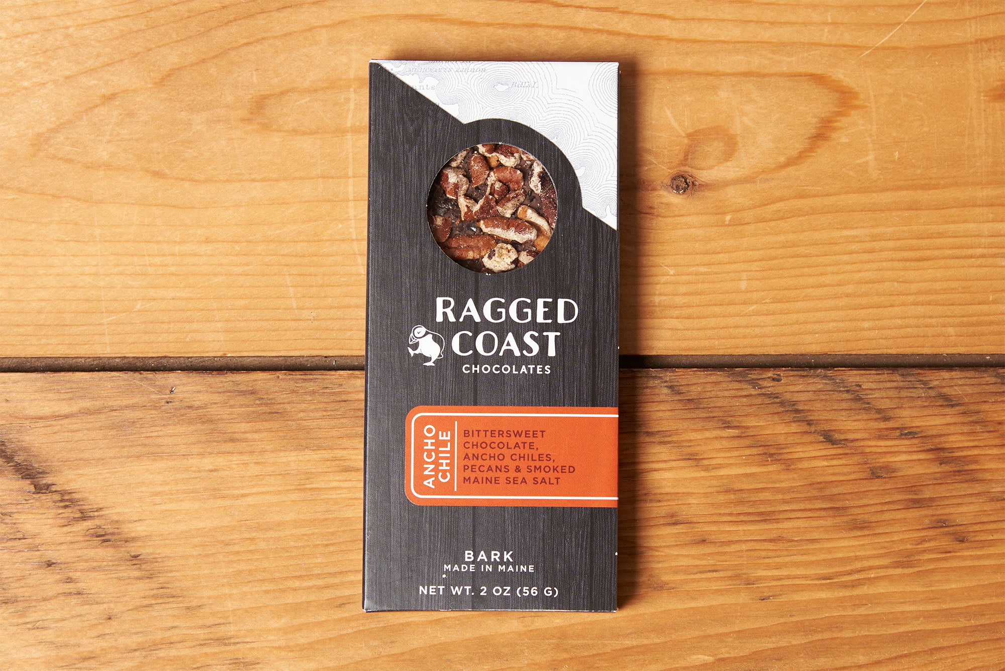 One Ragged Coast Chocolates Chocolate Ancho Chile and Roasted Pecan Bark sits on a wooden table.