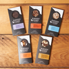 Assorted flavors of Ragged Coast Chocolates Chocolate Bark sit on a wooden table.