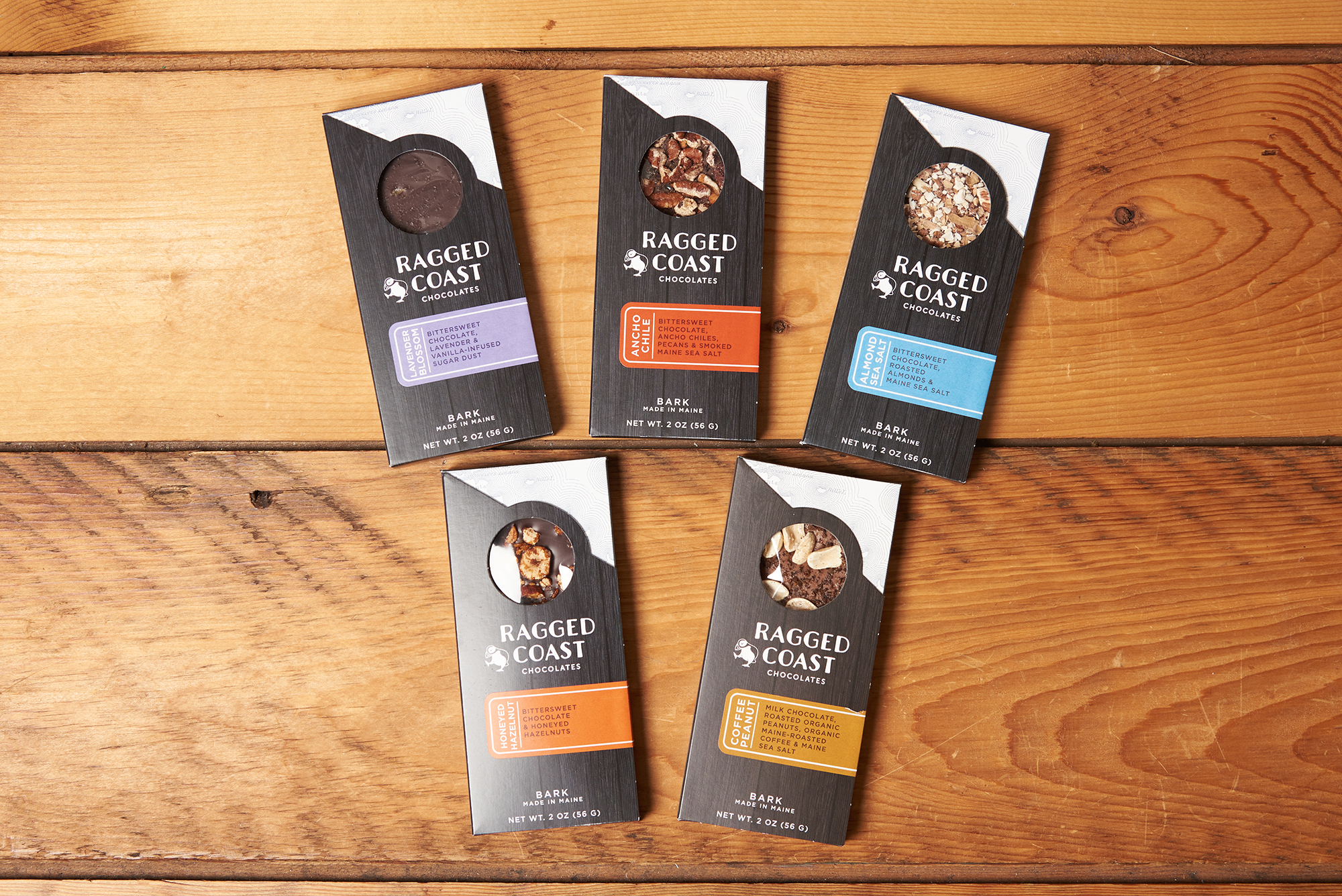 Assorted flavors of Ragged Coast Chocolates Chocolate Bark sit on a wooden table.