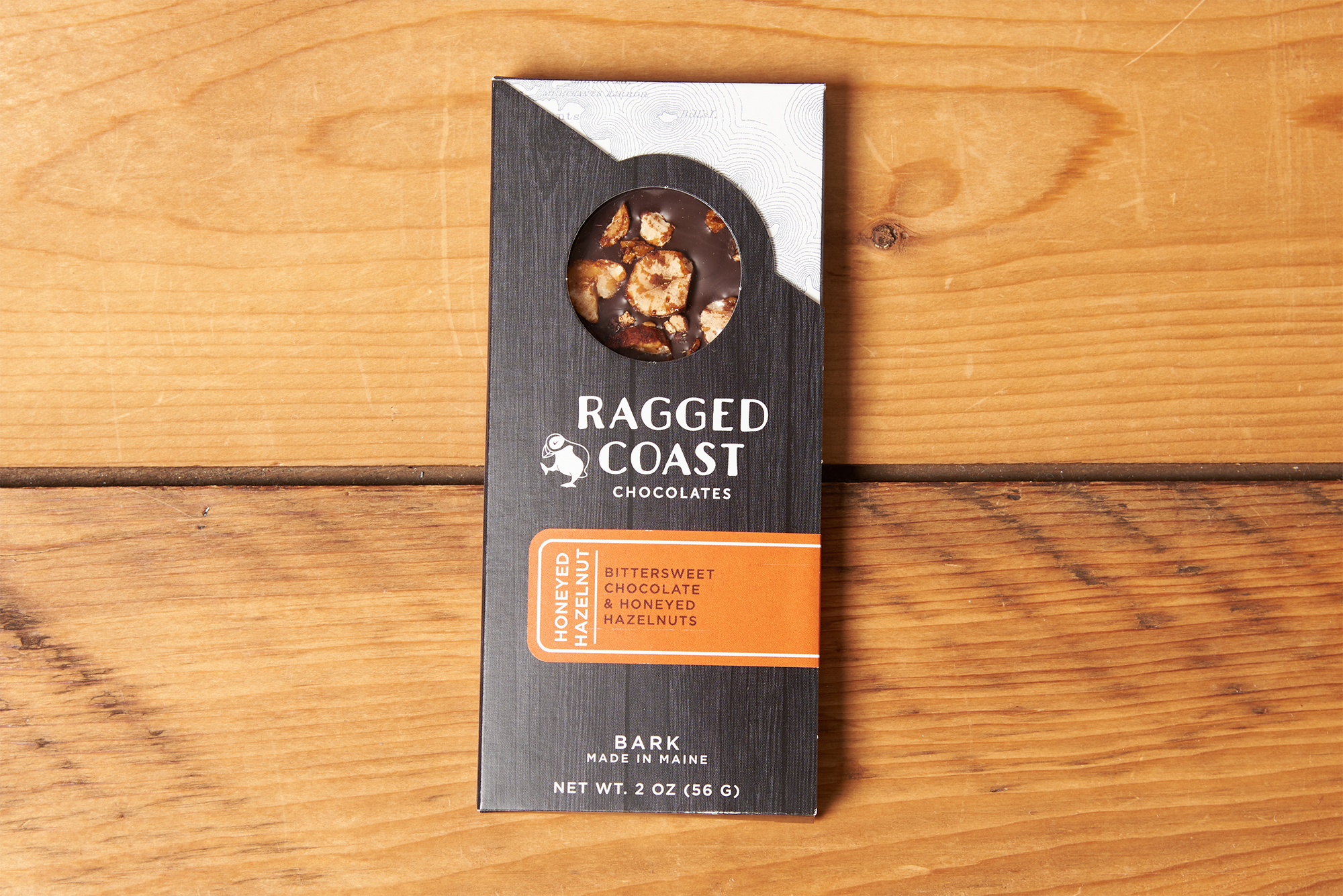 One Ragged Coast Chocolates Chocolate Honeyed Hazelnut Bark sits on a wooden table.