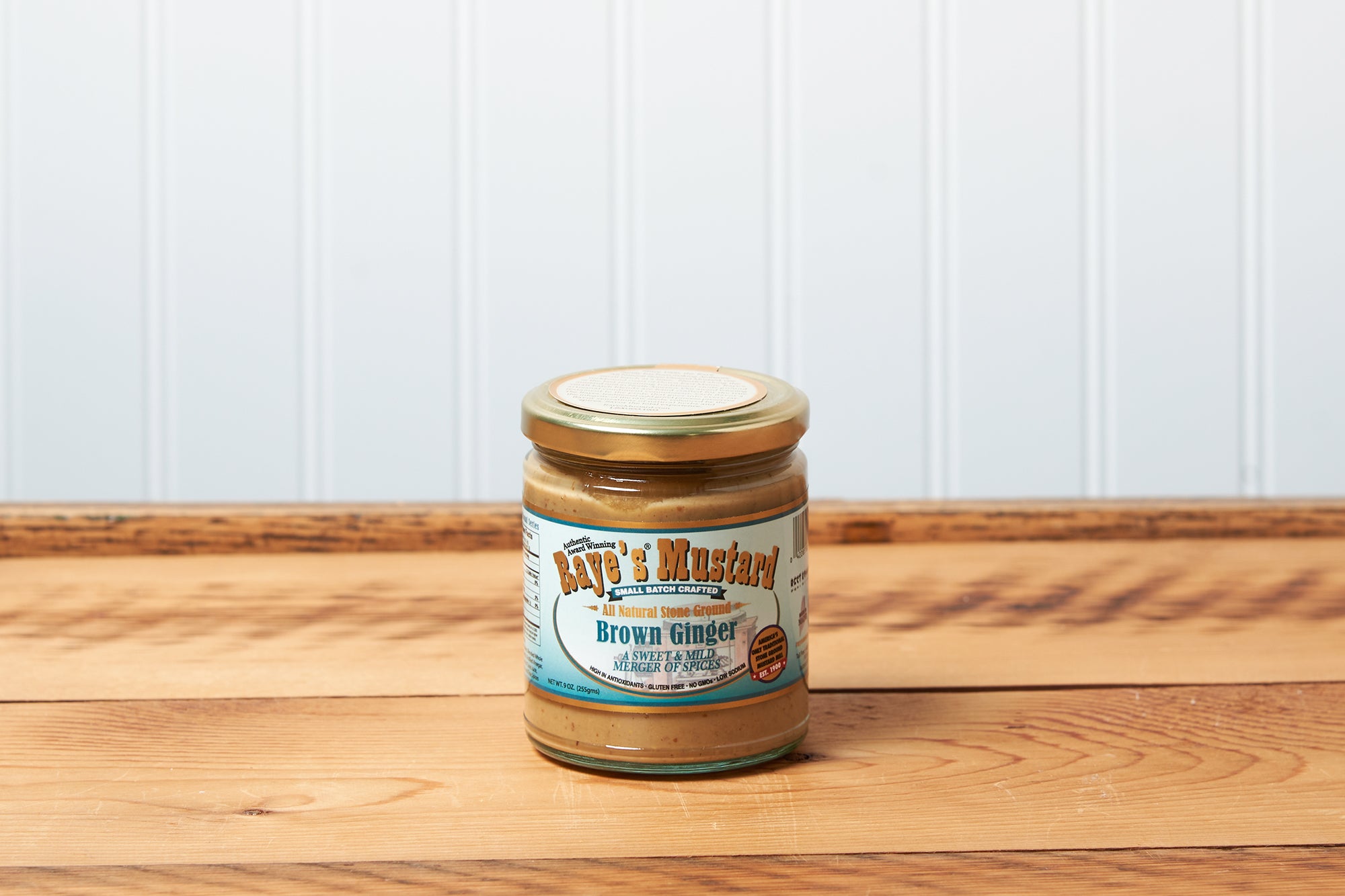 A jar of Raye's Brown Ginger Mustard sits on a brown wooden table.