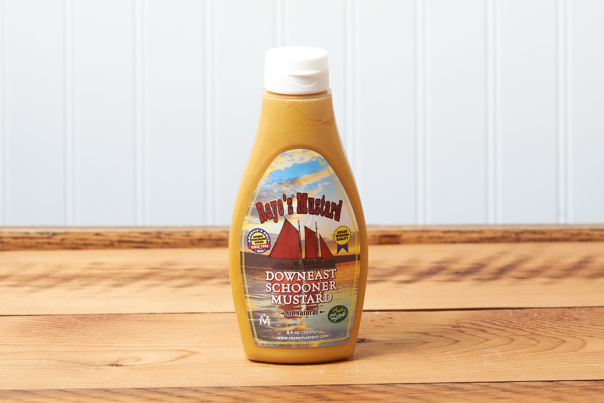 A bottle of Raye's Downeast Schooner Mustard sits on a brown wooden table.