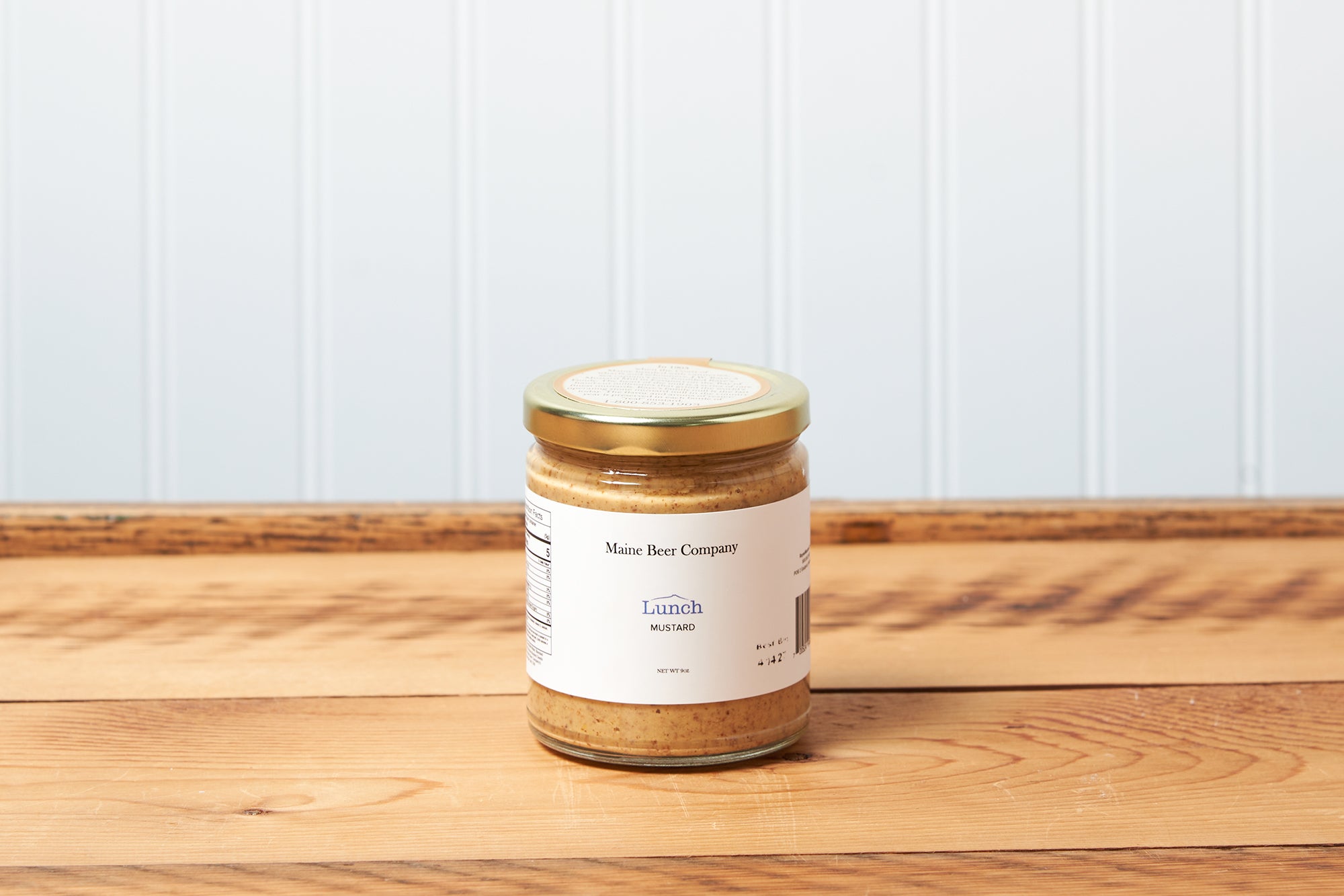 A jar of Raye's Maine Beer Company Lunch Mustard sits on a brown wooden table.